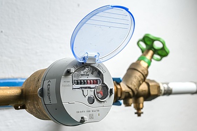 Ein Wasserzählers. Das runde, metallische Gerät zeigt ein Zifferblatt mit mehreren Zählwerken, die den Wasserverbrauch in Kubikmetern anzeigen.