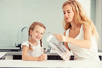 Eine Mama schenkt ihrem Kind Wasser in ein Glas.