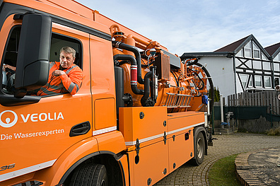 Ein Spülfahrzeug in auffälligem, leuchtendem Orange. Das Fahrzeug ist modern und robust gestaltet, mit einem großen Tank für Spülwasser und einer sichtbaren Spülvorrichtung.