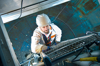 In einem Trinkwasser-Hochbehälter klettert ein Mitarbeiter von Veolia in Schutzkleidung mit weißem Helm eine Leiter hinab. Der leere, große Wasserspeicher wird für eine Wartung oder Inspektion begangen, der den Hygienevorschriften für Trinkwasserbehälter entspricht.