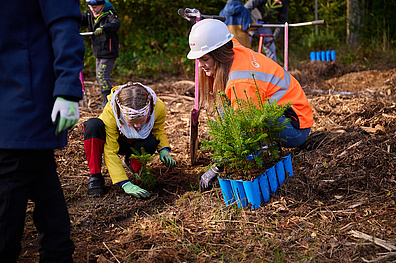 Eine Veolia Mitarbeiterin pflanzt gemeinsam mit einem Kind in einem Waldstück einen Baum im Rahmen eines Aufforstungsprojektes.
