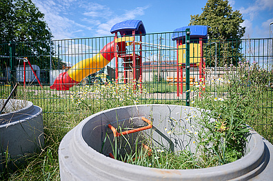 Grundhafter Ausbau in Gorschmitz (Stadt Leisnig). Hier werden ne Ein eingezäunter Kinderspielplatz im Freien. Im Mittelpunkt steht eine auffällige rot-gelbe Rutsche. Der Zaun umgibt den gesamten Spielbereich und sorgt für Sicherheit.