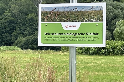 Ein Schild das am Wiesenrand steht. Auf dem Schild ist das Logo von Veolia zu sehen. Es zeigt, wie Veolia sich für den Artenschutz und Biodiversität einsetzt.