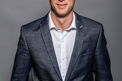 Porträt von Dr. Markus Biegel in Geschäftskleidung. Er trägt einen dunkles Jacket über einem weißen Hemd ohne Krawatte, was einen modernen, aber seriösen Eindruck vermittelt.