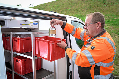 Ein Mitarbeiter von Veolia in Arbeitskleidung steht neben einem Dienstfahrzeug. Er platziert sorgfältig Wasserproben in einem speziellen Kühlraum im Fahrzeug.