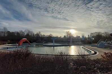 Freibad Rehau im Winter mit gefülltem großen Becken im Vordergrund mit Rutsche in winterlicher Stimmung