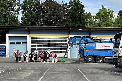 Veolia-Mitarbeiter und Kinder stehen neben Spezialfahrzeugen