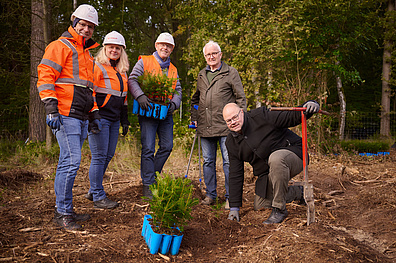 5 personen stehen im Wald und halten kleine tannen sowie Spaten in der Hand für ein Aufforstungsprojekt im Oschatzer Fliegerhorst.