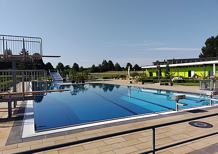 Fotoaufnahme vom großen Schwimmerbecken des Stadtbads Leisnig. Im linken Vordergrund die zwei Sprungtürme (1 Meter und 3 Meter). Im weiten Hintergrund die große Edelstahlrutsche.