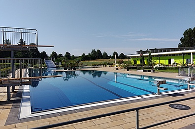 Fotoaufnahme vom großen Schwimmerbecken des Stadtbads Leisnig. Im linken Vordergrund die zwei Sprungtürme (1 Meter und 3 Meter). Im weiten Hintergrund die große Edelstahlrutsche.