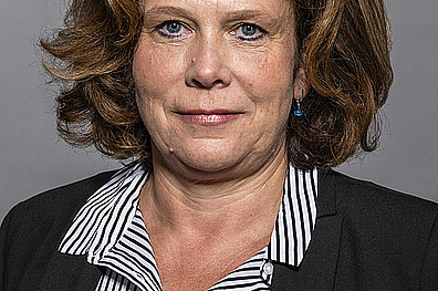 Porträt von Kerstin Härtel. Sie hat schulterlanges, welliges braunes Haar und trägt eine schwarz-weiß gestreifte Bluse. Sie lächelt leicht in die Kamera.