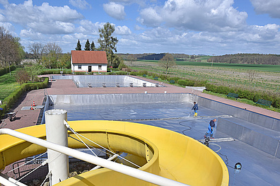Das Bild wurde auf der Wasserrutsche aufgenommen: Im Zentrum des Bildes ist das große Schwimmbecken zu sehen. Die Reinigungsarbeiten im Schwimmbecken laufen auf Hochtouren.