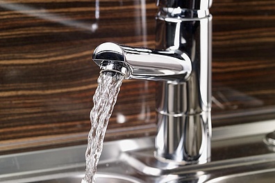 Nahaufnahme eines geöffneten Wasserhahns. Aus der glänzenden Metallarmatur fließt ein klarer Wasserstrahl.