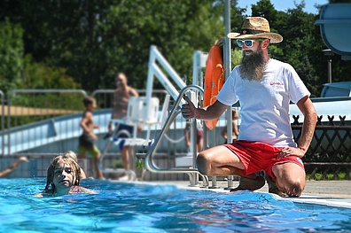 Ein Bademeister mit einem Sonnenhut und Sonnenbrille beaufsichtigt die Kinder im Schwimmkurs.