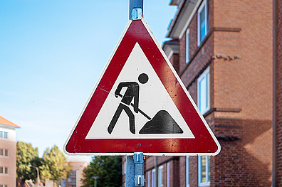 1177059051 Ein dreieckiges Baustellenschild mit rotem rand zeigt das Symbol eines Bauarbeiters mit einer Schaufel.