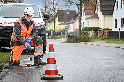 Veolia-Mitarbeiter in Warnweste und Schutzhelm kniet auf einer Straße und setzt ein Messgerät zur Leckortung an einem Bodenpunkt an.