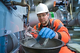 Im Wasserwerk hält ein Mitarbeiter eine Karaffe mit Wasser in der Hand. Er nimmt eine Wasserprobe.