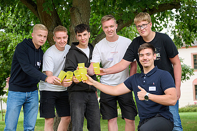 Ein Gruppenfoto von sechs jungen männlichen Azubis, die in die Kamera lächeln. Jeder von ihnen hält einen gelben Veolia Becher in der Hand zur Kamera hin.