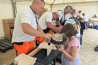 An einem langen Tisch stehen Veolia-Mitarbeiter und Grundschulkinder zusammen. Gemeinsam montieren sie aus Holzbausätzen Vogel- und Fledermauskästen.