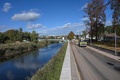 Blick entlang der Sörmitzer Straße in Döbeln während der Bauarbeiten: Links fließt die Mulde als Kanal, rechts verläuft die Baustelle mit einem gelben Baufahrzeug.