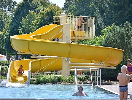 Die große gelbe Wasserrutsche vom Muldentalbad Kleinbothen. Die Rutsche hat zwei Ebenen mit geschwungenen Bahnen. Am unteren Ende mündet sie in ein Wasserbecken. Im Hintergrund sind Bäume und ein Gebäude zu sehen.