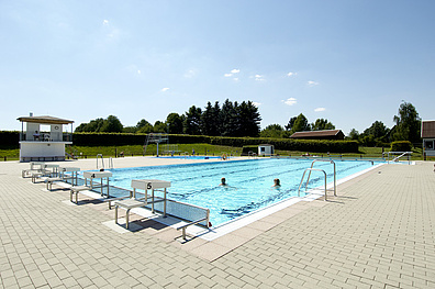 Das Freibad Geithain mit einem großen, rechteckigen Schwimmbecken, das in mehrere Bahnen unterteilt ist. Um das Becken herum erstreckt sich eine gepflasterte Fläche.