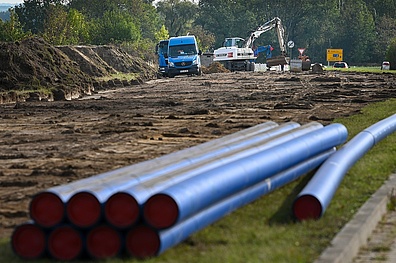 Mehrere blaue Polyethylen-Rohre für die Bauarbeiten der Trinkwasserleitungen. Im Hintergrund: Eine Baustelle mit typischen Baustellenfahrzeugen.