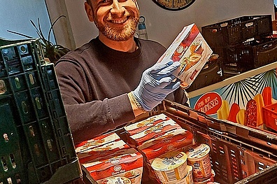 Ein junger Mann sortiert Lebensmittel. Vor ihm stehen Kisten mit Joghurt und anderen Milchprodukten.
