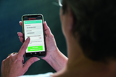 Das Bild zeigt einen Mann von hinten, der ein Smartphone in seiner Hand hält. Auf dem Bildschirm des Smartphones ist die Website geöffnet, die es dem Nutzer ermöglicht, Wasserzählerstände online einzugeben.