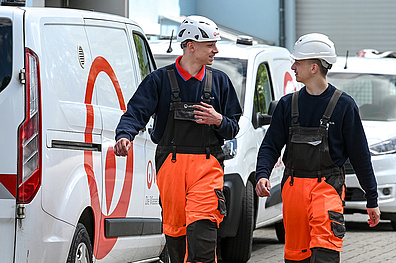 Zwei junge Männer in Arbeitskleidung. Im Hintergrund weiße Autos mit Veolia-Logo.